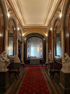 an ornate hallway with statues on either side and stained glass windows in the back ground