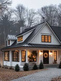 a white house with black shingles and lights on the front door is surrounded by trees