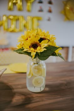 a vase filled with lemon slices and a sunflower on top of a wooden table