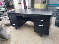 a black desk sitting on top of a floor next to a pile of boxes and bins