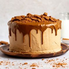 a cake with chocolate icing and nuts on top sitting on a plate next to a glass of milk