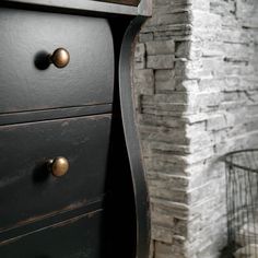 a black dresser with two drawers next to a brick wall