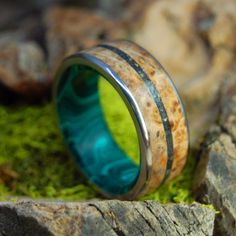 a wooden ring with blue and green inlays on top of moss covered rocks