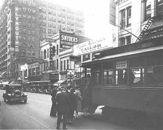 an old black and white photo of people standing on the sidewalk near a trolley car