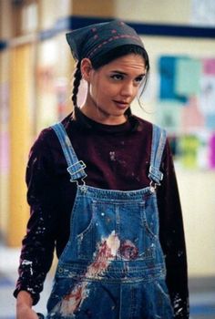 a woman in overalls and a bandana is walking down the street with her hand on her hip