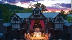 an aerial view of a large building with people on stage in the center and mountains in the background