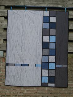 two quilts hanging on the side of a brick wall next to a wooden fence