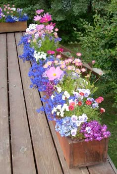 several flower boxes are lined up on a wooden deck in front of some bushes and trees