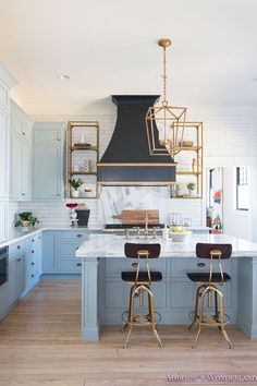 two stools sit in front of an island with marble countertops and blue cabinets