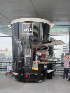 a black food truck parked in front of a building with people standing around it and talking on their cell phones