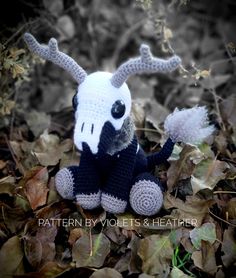 a crocheted stuffed animal with horns and antlers sitting on leaves in the woods