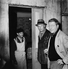 black and white photograph of three men standing in an unfinished room with one looking at the camera