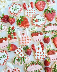 some decorated cookies are sitting on a white table with strawberries and strawberrys around them