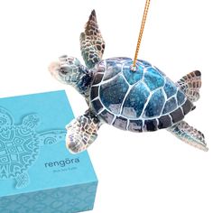 a small turtle ornament hanging from a string next to a blue gift box