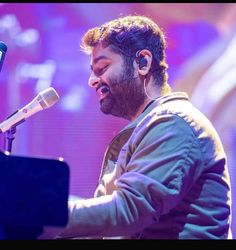 a man with headphones on singing into a microphone while holding a piano in front of him