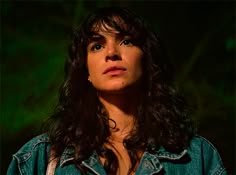 a woman with long dark hair wearing a jean jacket and looking up at the sky