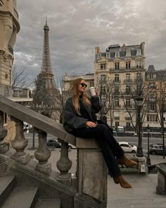 a woman sitting on top of a stone railing next to a building with the eiffel tower in the background