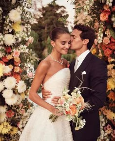 a bride and groom standing in front of a floral arch with flowers on it's sides