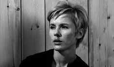 a black and white photo of a woman in front of a wooden wall looking at the camera