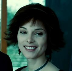 a woman with short hair smiling and wearing a black dress in front of a window