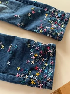 two pairs of blue jeans with multicolored stars on them