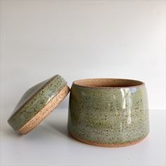 two green cups sitting next to each other on a white counter top, one has a lid and the other has a brown rim