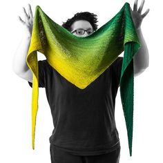 a woman is holding up her green and yellow shawl over her head with both hands