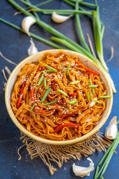 a bowl filled with noodles and vegetables on top of a blue tablecloth next to green onions