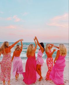 four women in pink dresses standing on the beach with their arms around each other's shoulders