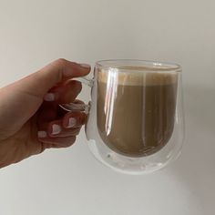 a hand holding a glass cup with liquid in it on a white table next to a wall