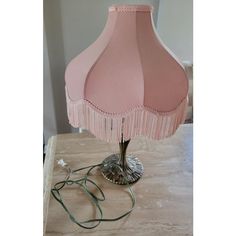 a pink lamp with fringes on it sitting on a table next to a wall