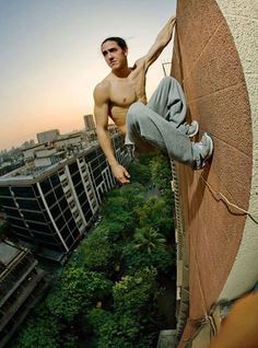 a shirtless man climbing up the side of a building with trees in front of him