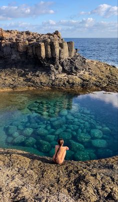 a person sitting on the edge of a body of water with rocks in the background