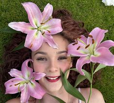 a woman laying in the grass with pink lilies on her head and eyes closed