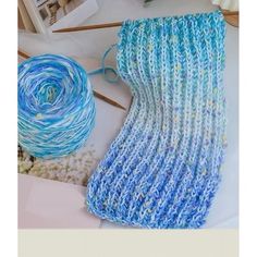 a blue and white knitted blanket next to a ball of yarn on a table