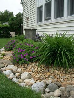 a garden with rocks and flowers in front of a house