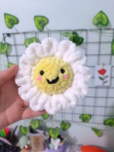 a hand holding a small crocheted flower with a smiley face on it's center