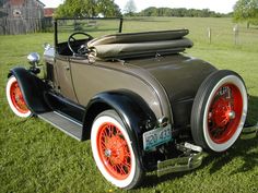 an old model t car is parked in the grass with orange rims on it