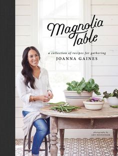 a woman sitting at a table in front of a potted plant on the cover of her book, magnolia table