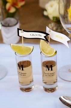 two shot glasses with lemon wedges in them on top of a white table cloth