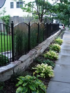 a black iron fence next to a sidewalk with flowers and plants growing on the side