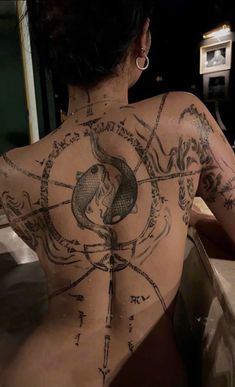 a woman with tattoos on her back sitting in a bathtub