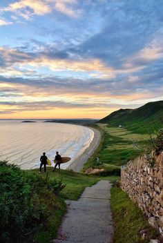 two people with surfboards walking down a path to the beach at sunset or dawn