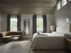 a bed room with a neatly made bed next to two windows and a chair in the corner