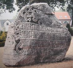 a large rock with writing on it in front of a tree and house behind it