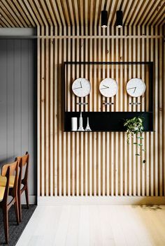 three clocks mounted on the wall in a room with wooden paneling and two chairs