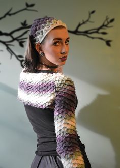 a woman wearing a knitted scarf in front of a tree with branches on it