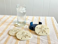 three sand dollar coasters sitting on top of a table next to a glass of water