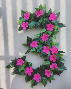 pink flowers are arranged in the shape of a letter s on a white surface with green leaves