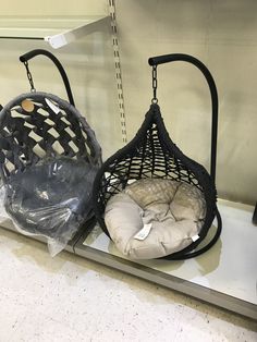 two hanging chairs with cushions on them in a store display case, one is black and the other is white